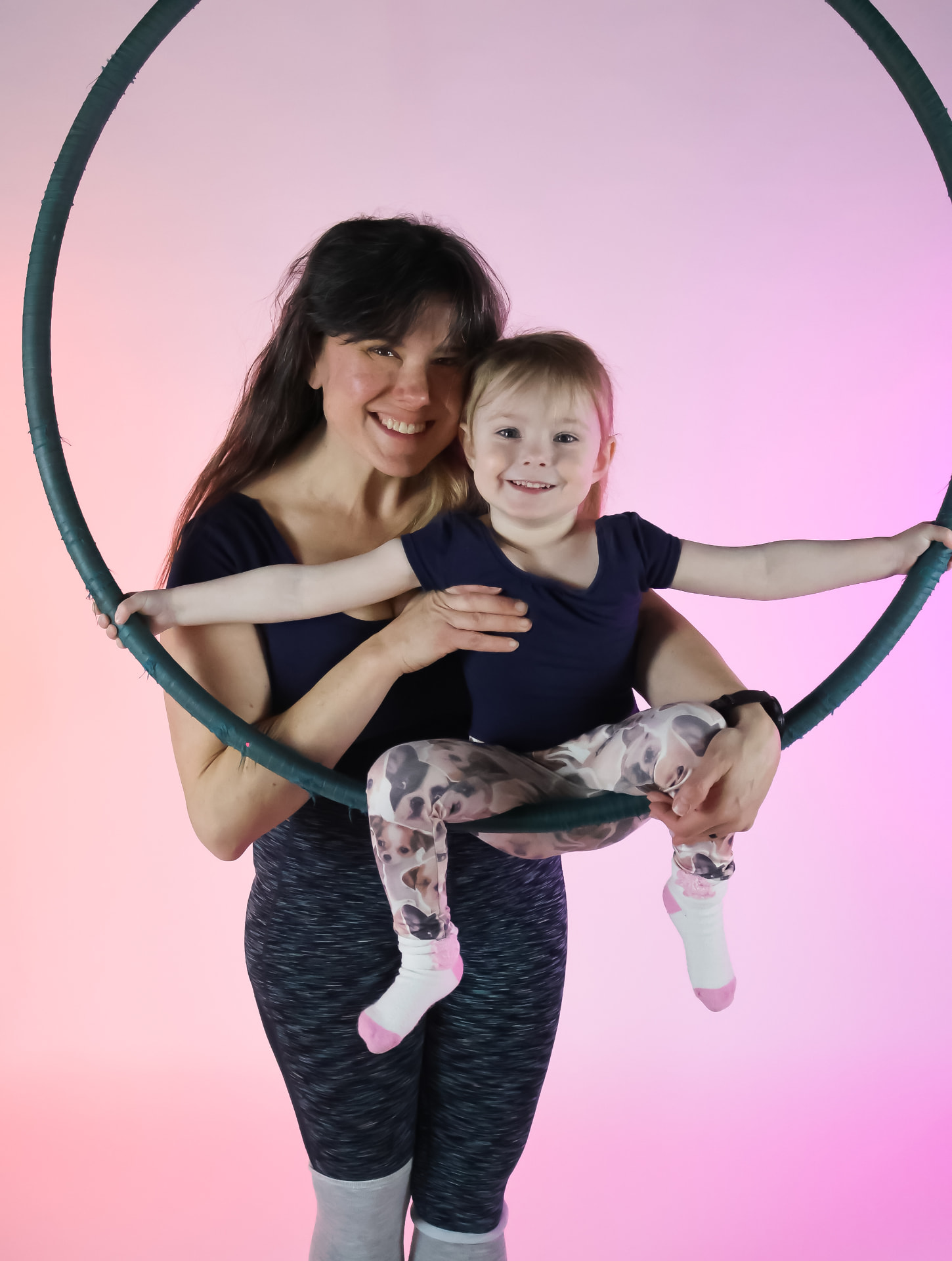 A mom and her young daughter smiling inside a lyra hoop during a family aerial class